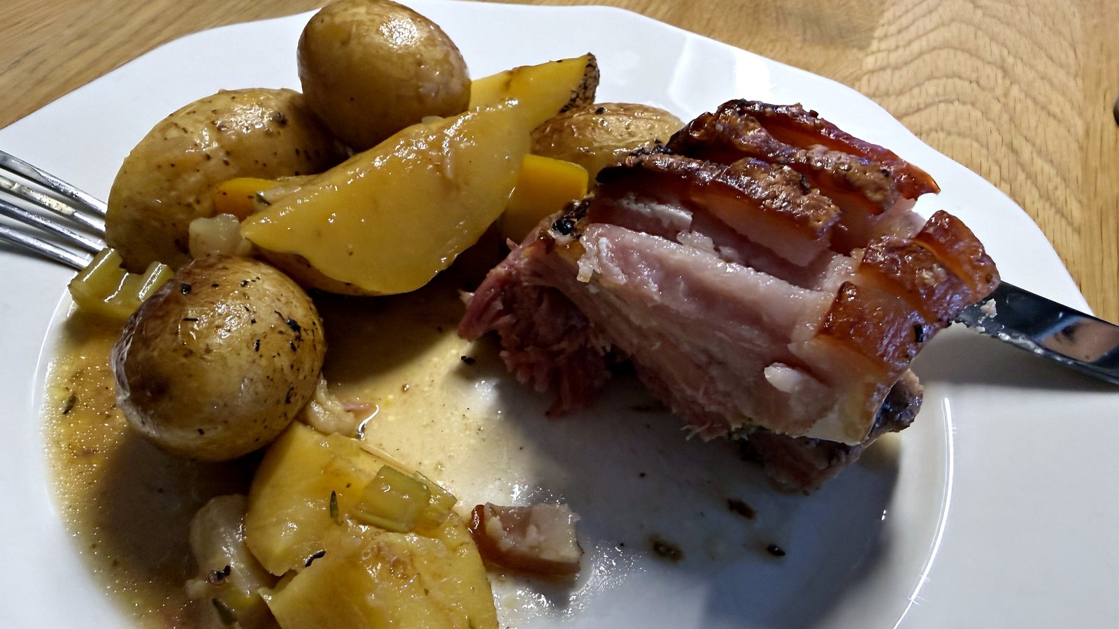 Ein Teller mit einer Scheibe Surbraten mit dunkler Kruste, kleinen Erdäpfeln mit Schale und etwas Saft.